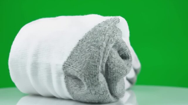 Rolled white sock with grey heel and toe against a green backdrop