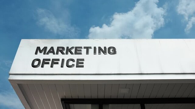 A marketing office word sign prominently displayed on a sleek corporate building under a clear blue sky, symbolizing branding, strategy, advertising, and promotion