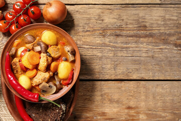 Bowl of tasty beef stew with ingredients and bread slices on wooden background