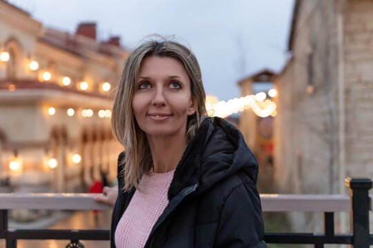 Woman smiling city beautiful adult standing outdoors in a European street illuminated by warm string lights at dusk