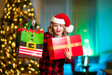 Child holding Christmas gift. Kid in Santa hat with winter holiday present. Child holding present...