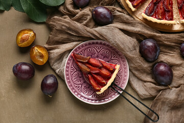 Plate with piece of tasty plum pie, spatula and fresh fruits on brown background