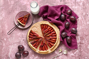 Tasty plum pie with spatula, fresh fruits and bottle of milk on pink grunge background