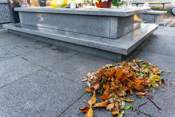 Pile of autumn leaves collected beside granite gravestone in cemetery, cleaned memorial area during seasonal maintenance on an autumn day