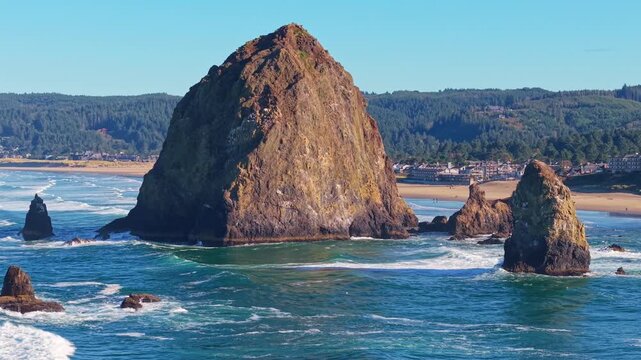 A stunning high-angle video capturing the iconic Haystack Rock and Cannon Beach shoreline bathed in the warm, golden, and vibrant hues of a sunset over the Pacific Ocean