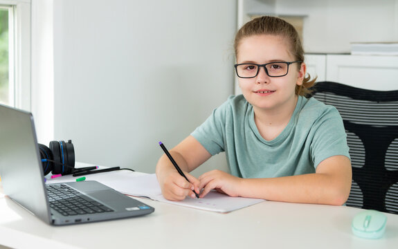 Kid using laptop for online studying at home. Child sitting at desk with laptop on virtual school lesson. Child learning with laptop. Young student . Kids watch online class on laptop.