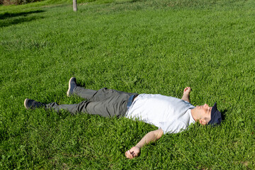 Side view photo of a middle aged man relaxing on the grass at a park. Top view photo.