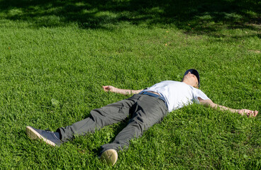 A middle aged man is relaxing lying on the grass at a park. Top view photo.