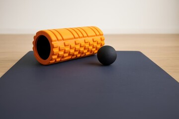 Foam roller and massage ball centered on a fitness mat. Essential equipment for self-myofascial release during workouts.