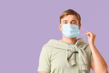 Happy young man wearing medical mask on purple background