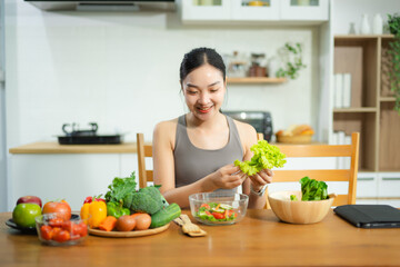 Asian woman prepares fresh vegetable salad in home kitchen. Healthy lifestyle, clean eating, wellness, and fitness food prep concept.