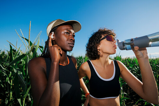 Friends exercising outdoors, hydrating and using wireless earbuds