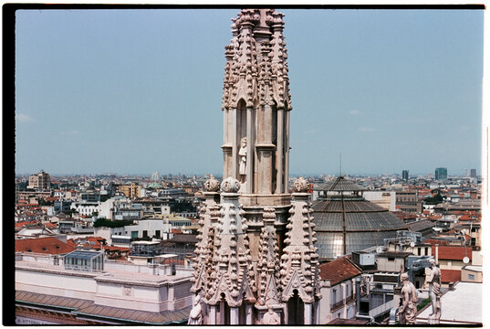 gothic spire of the Milan Cathedral rooftop over cityscape, 35mm film