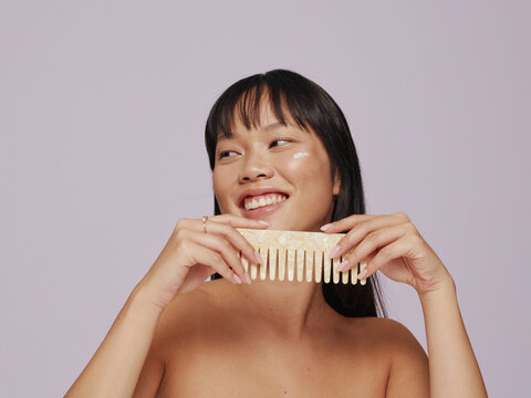 Smiling Woman Holding a Wooden Comb in a Soft Pastel Setting