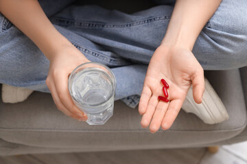 Young woman with vitamin E pills and glass of water in armchair at home, top view