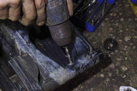 Close up of skilled mechanic hand drilling hole in black plastic component for repair. focused worker using power tool for maintenance work inside garage workshop