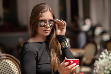 Sunglasses Coffee Woman: Outdoor cafe, lady relaxes holding cup, adjusts sunglasses, summer afternoon.