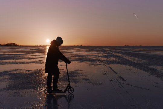 Person rides a scooter on ice during sunset