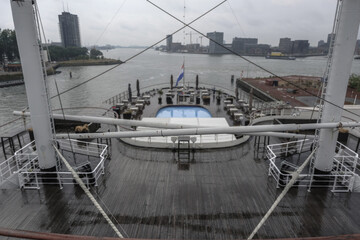 Outdoor decks of classic historic ocean liner cruiseship cruise ship with wooden teak planks, life boat promenade and swimmingpool wet with rain superstructure silhouette