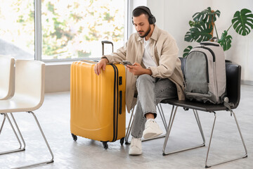 Young man in headphones with mobile phone waiting for his flight in airport lounge