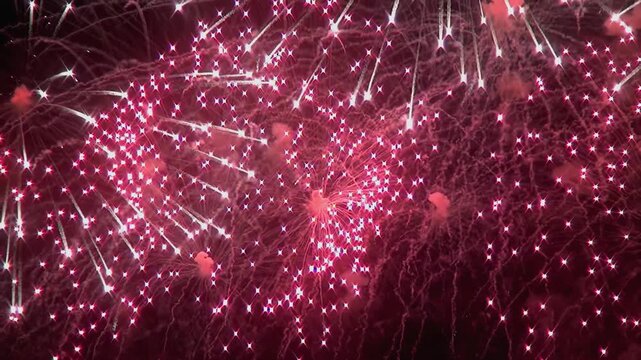 Vibrant ruby fireworks burst and bloom in the darkness, painting star-like patterns across the heavens. A dazzling display of light and sound for a nighttime celebration.