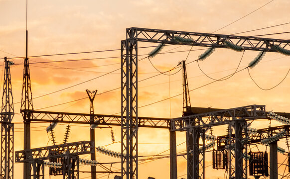 Sunset over power station with transmission towers and electrical equipment in silhouette