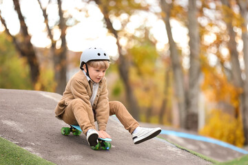 Cute little boy with helmet riding skateboard in park on autumn day
