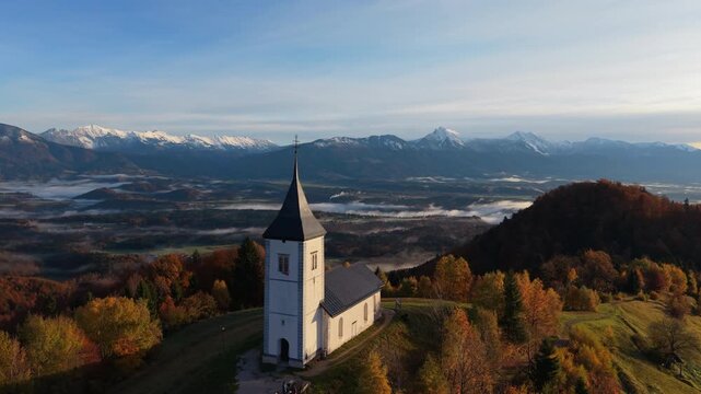 Beautiful aerial view of Saint Primus church on a hill in Jamnik, Slovenia with mountains and autumn colors.