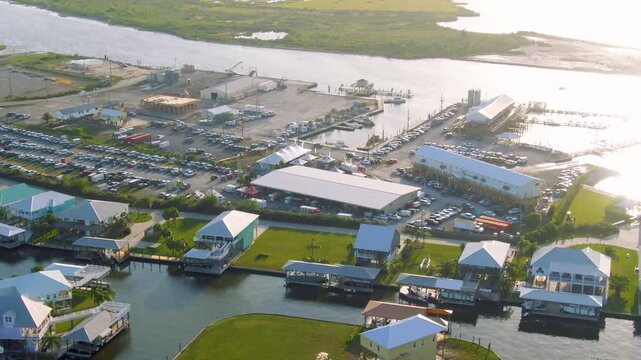 Wide aerial over Grand Isle, Louisiana, during the festival showing Bayou Fifi, Fifi Island, the marina, stilt homes, green grass, a full parking lot, and a boat gliding through calm coastal water.