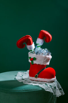 elf legs inside a santa boot on a green velvet stool