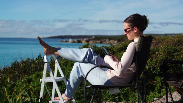 Woman reading an e-reader in a beach chair by the coast