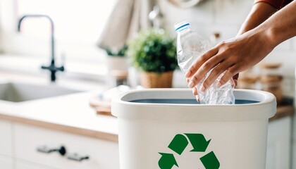 Hands recycling a plastic bottle into a bin with a green symbol in a modern kitchen