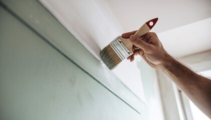Hand with paintbrush applying fresh green paint to a wall during home renovation