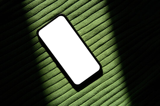 Smartphone With White Screen on Green Fabric Under Bright Light