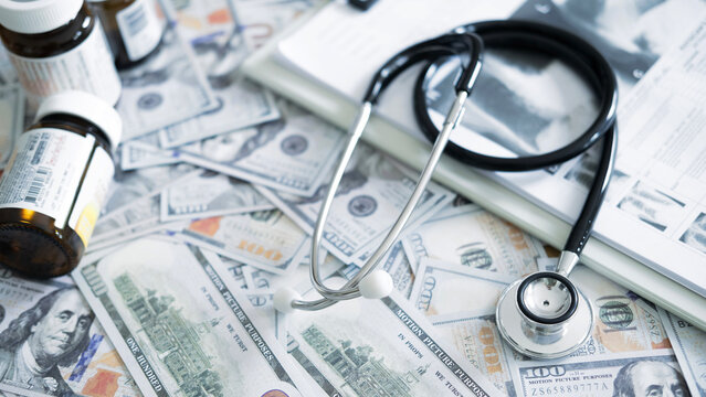 Medical files and stethoscope on top of currency showing cost of diagnosis, medical analysis expenses and healthcare economic pressure.