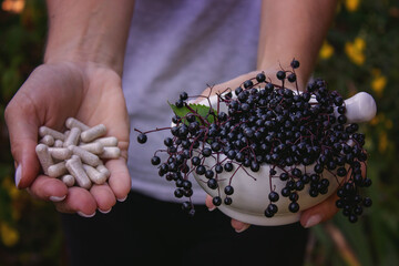 Woman's hands holding elderberry: berries, syrup and capsules. Healthy nutrition.