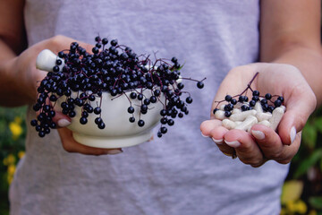 Woman's hands holding elderberry: berries, syrup and capsules. Healthy nutrition.
