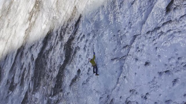 Alpinist ice climbing an immense frozen glacier wall