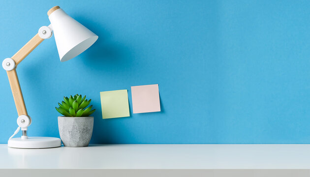 Minimalist workspace with white lamp, succulent, and sticky notes against a blue wall.