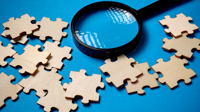 Search for the Missing Piece: Magnifying Glass Inspecting Wooden Jigsaw Puzzle on a Vibrant Blue Background
