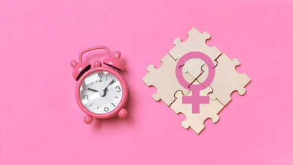 Women's Biological Clock: Pink Alarm Clock Next to Jigsaw Puzzle Forming the Female Gender Symbol...