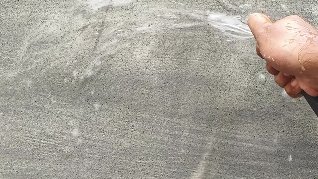 Closeup of Indian person hand with garden hose pouring water to wet new building cement wall surface after initial construction for preventing cracks, adding strength and stop curing.