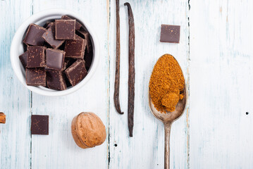 pile of brown sugar on old spoon, vanilla, broken dark chocolate blocks on white wooden table