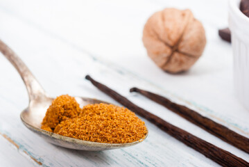 pile of brown sugar on old spoon, vanilla, broken dark chocolate blocks on white wooden table