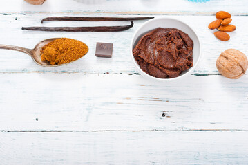 pile of brown sugar on old spoon, vanilla, broken dark chocolate blocks on white wooden table