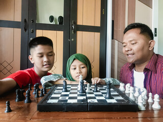 A dad enjoys playing chess with his kids at home
