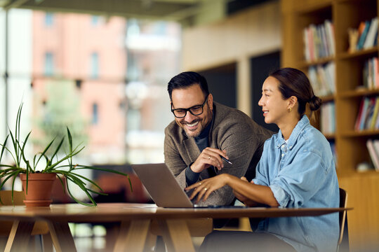 Fototapeta Asian Woman And Man Collaborate At Library Table Using Laptop For Friendly Business Project