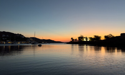 Peaceful sunset view over Vourkari harbor within Kea, also known as Tzia, featuring calm waters, moored sailboats, and warm evening light reflecting upon the serene Aegean Sea horizon