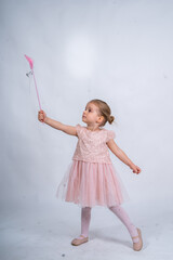 Rear view of a little girl in a pink tutu and ballet slippers, standing gracefully with a tiara on her head, holding pointe shoes.Little ballerina practicing dance moves. 