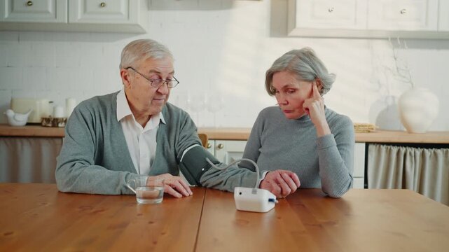 Aged man and woman using modern electronic monitor for measuring blood pressure. Healthcare and body condition control in old age, careful wife and sick man, risk of insult and heart attack after 60